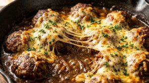 Ultra close-up of bubbling skillet with creamy French onion beef meatballs in rich caramelized onion gravy topped with melted golden Gruyere cheese